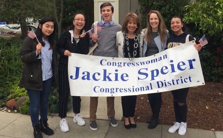 Five students with congresswoman holding up sign and American Flags, sign says "Congresswoman Jackie Speier Congressional District"